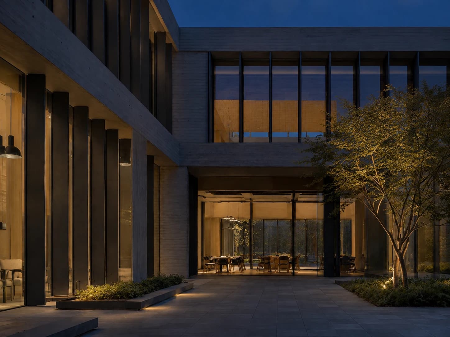 The same office courtyard at blue hour, with warm interior lighting and changing reflections