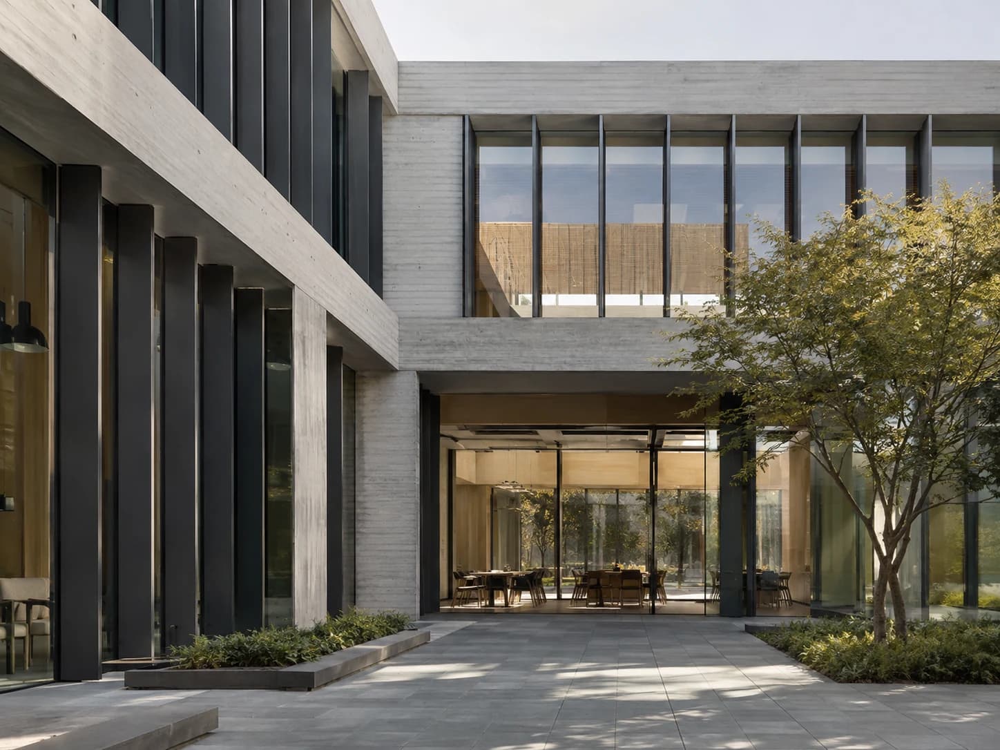 Concrete and glass office courtyard in daylight, with sunlight falling across the stone paving